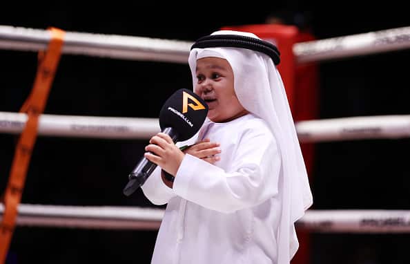 Abdu Rozik wearing white robe and head covering while holding a microphone in a boxing ring