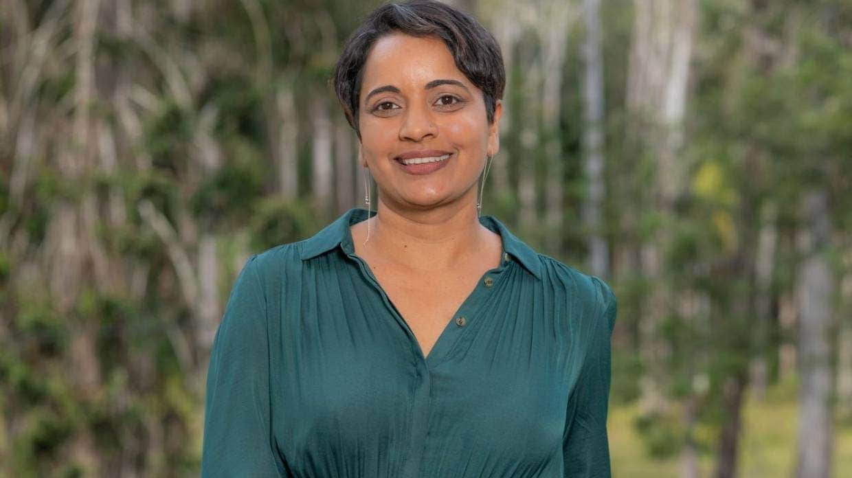 A woman with a teal shirt standing in front of some trees
