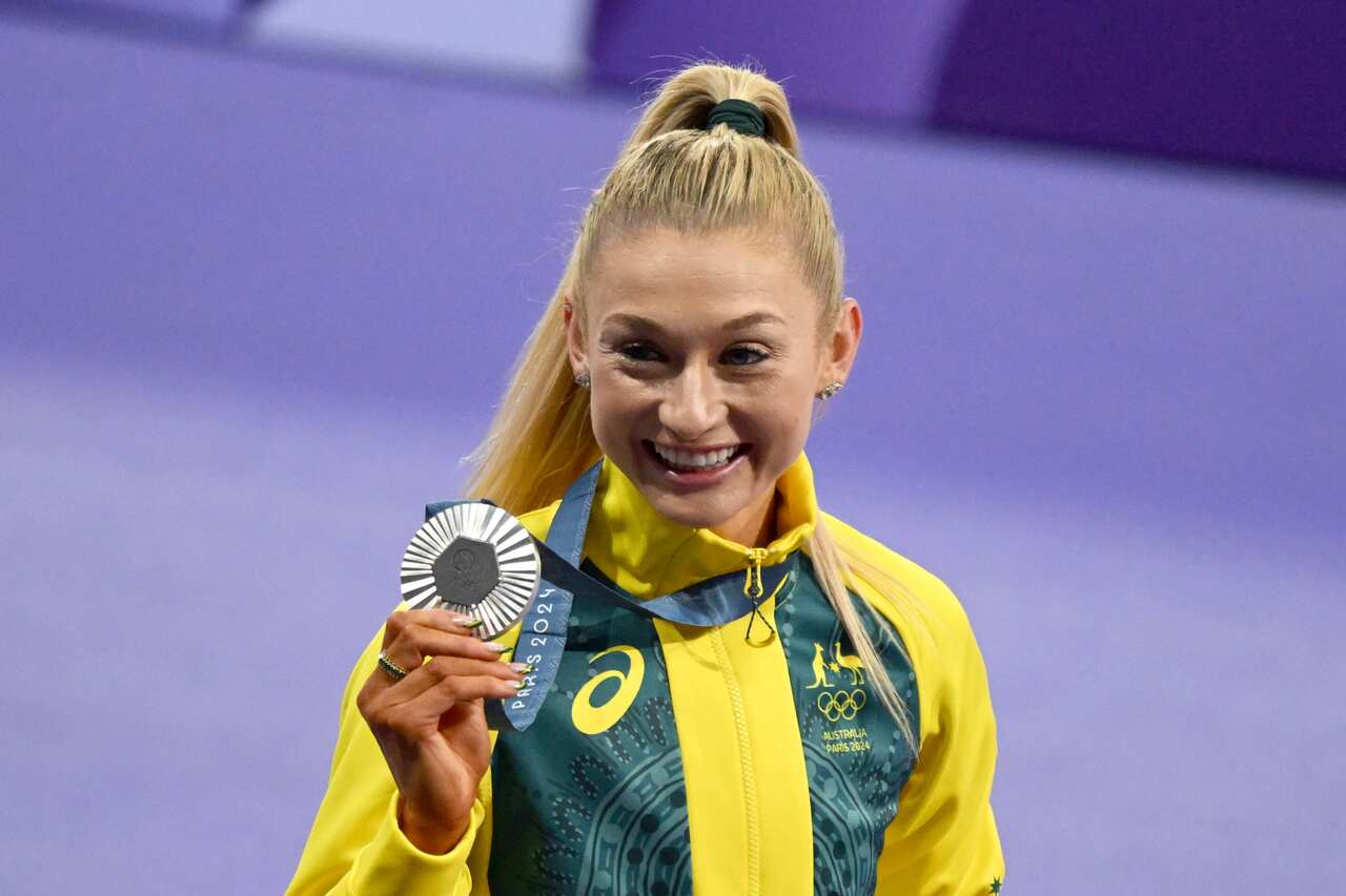 A woman wearing a green and gold jacket smiling and holding a silver medal