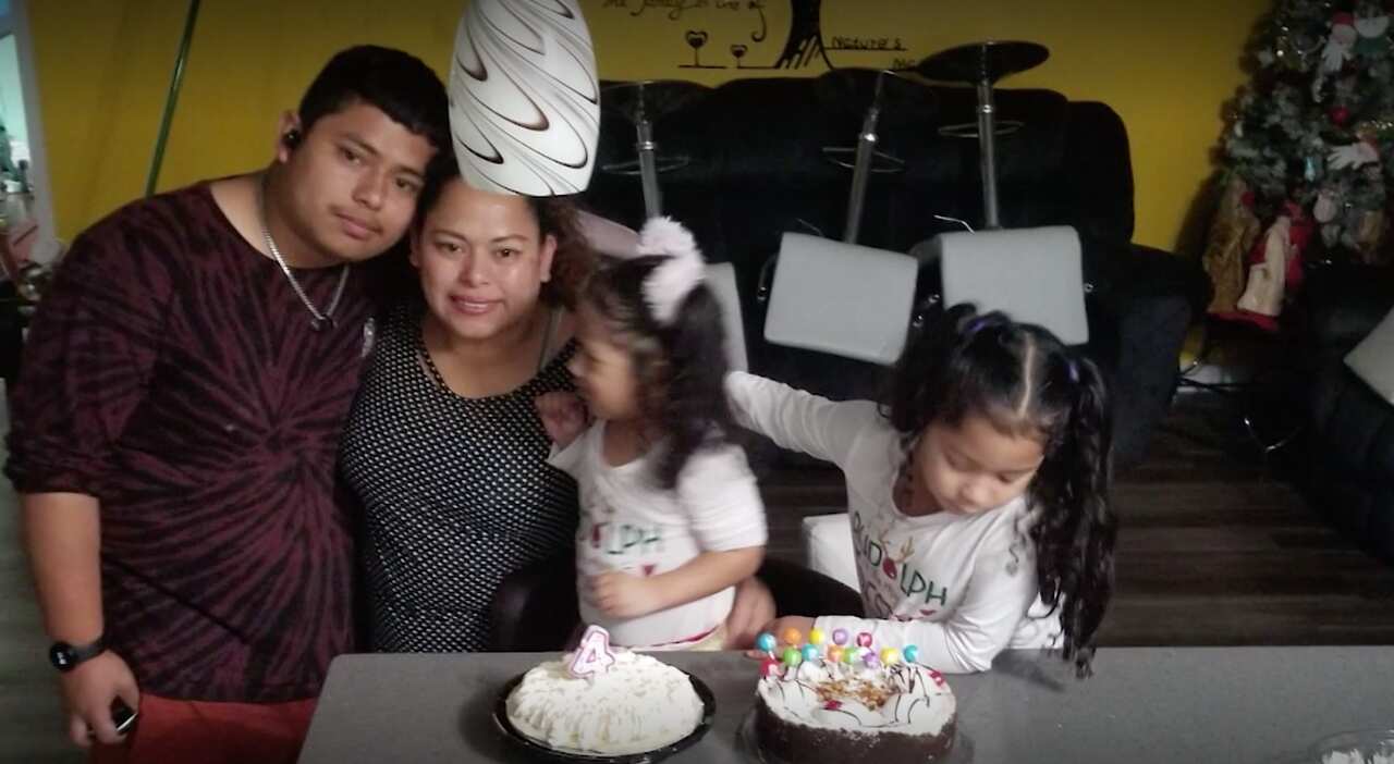 A family stands in front of a birthday cake. 