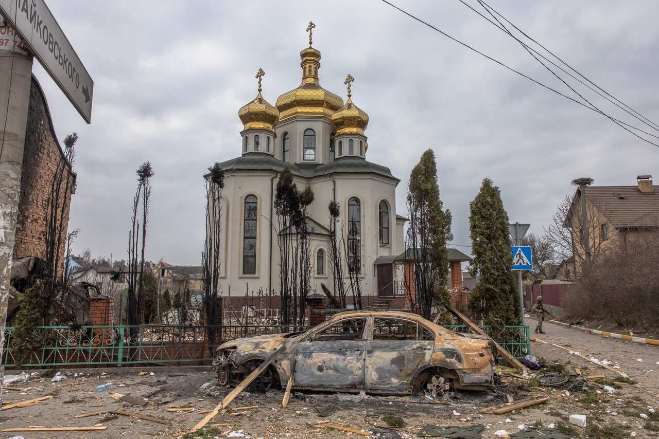A Ukrainian military member is seen standing guard next to a damaged church.