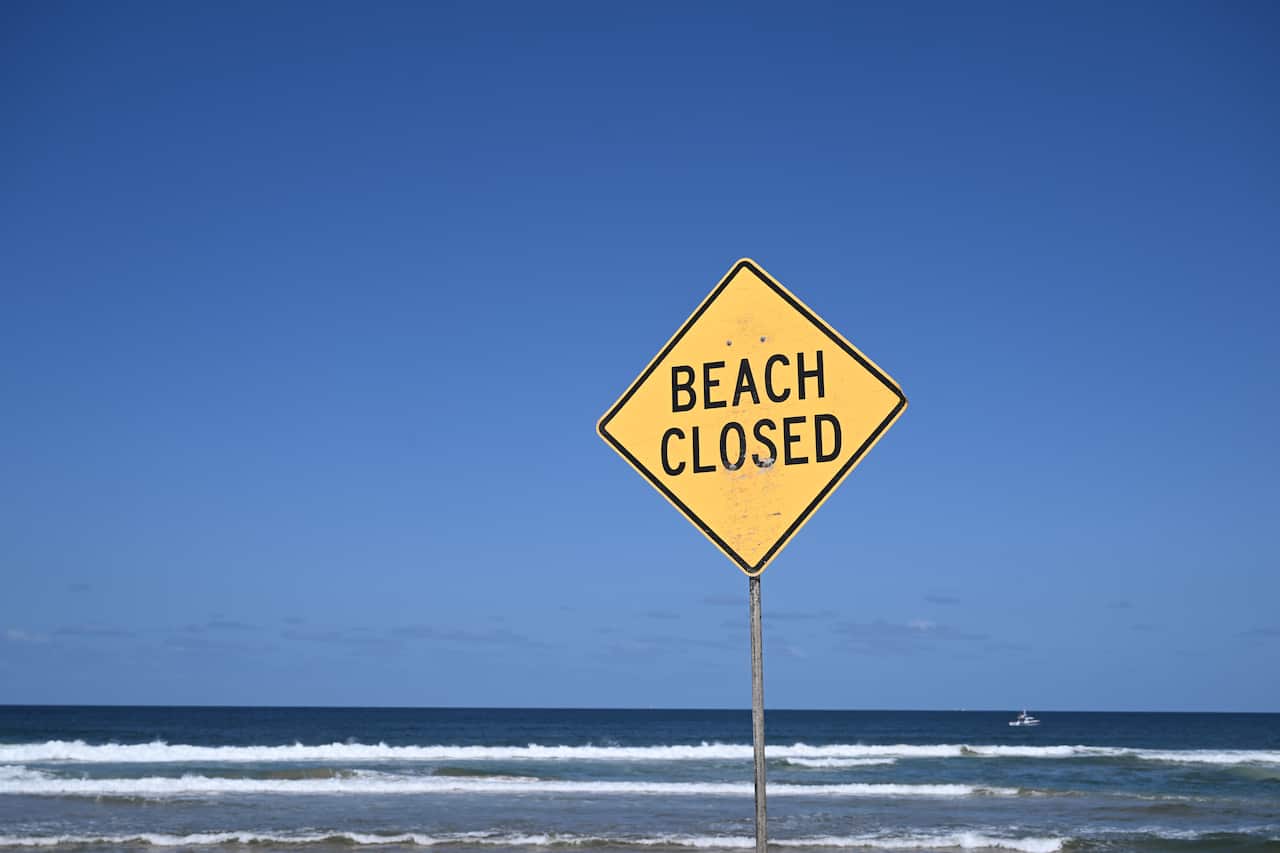 A sign saying "beach closed" in front of blue and white waves breaking.