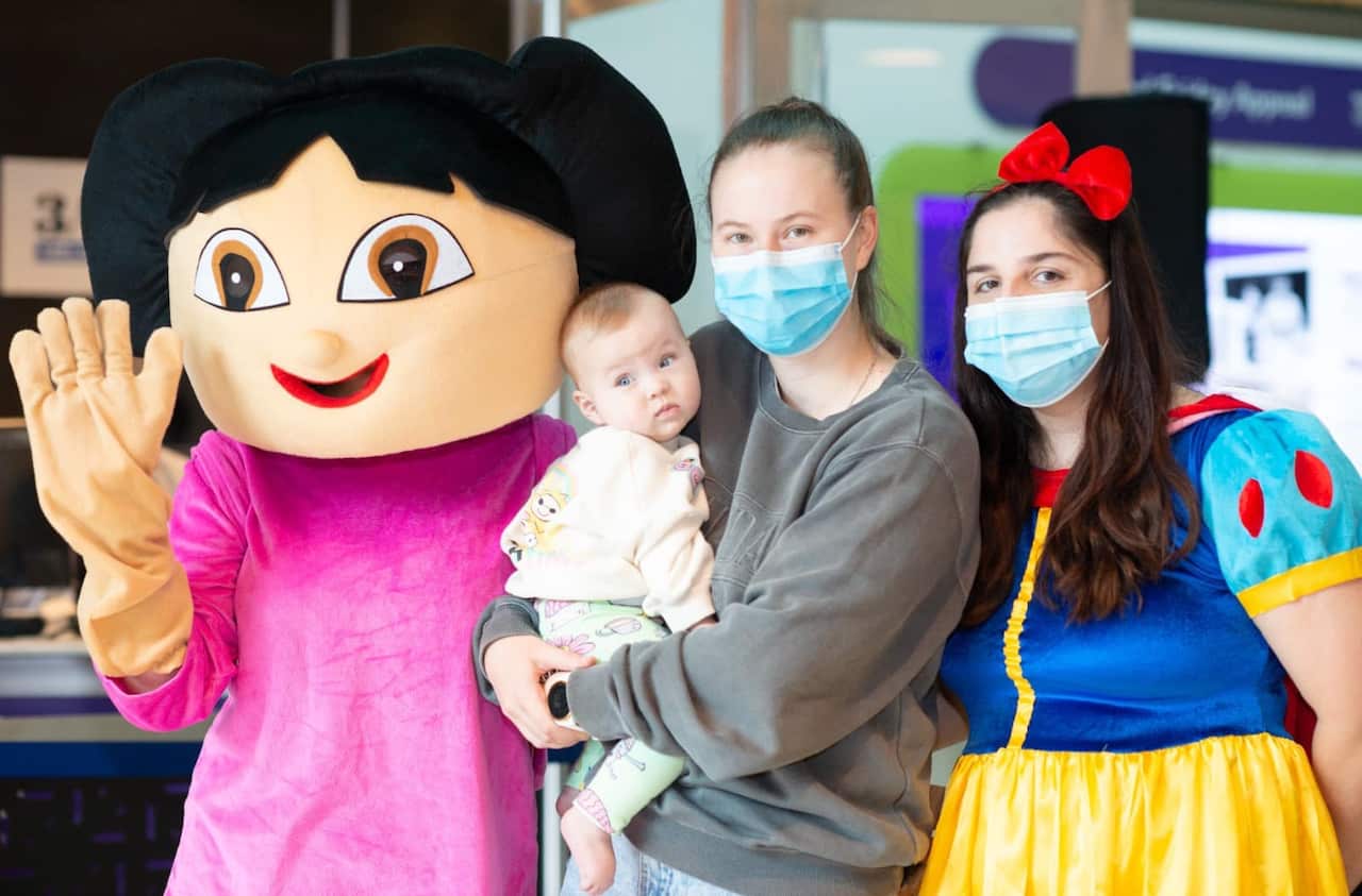 As part of the hospital's Good Friday Appeal, people dressed up in costumes from children's shows. Here, there is a snow white costume and a Dora the Explorer costume. A mother is also shown holding her infant child.