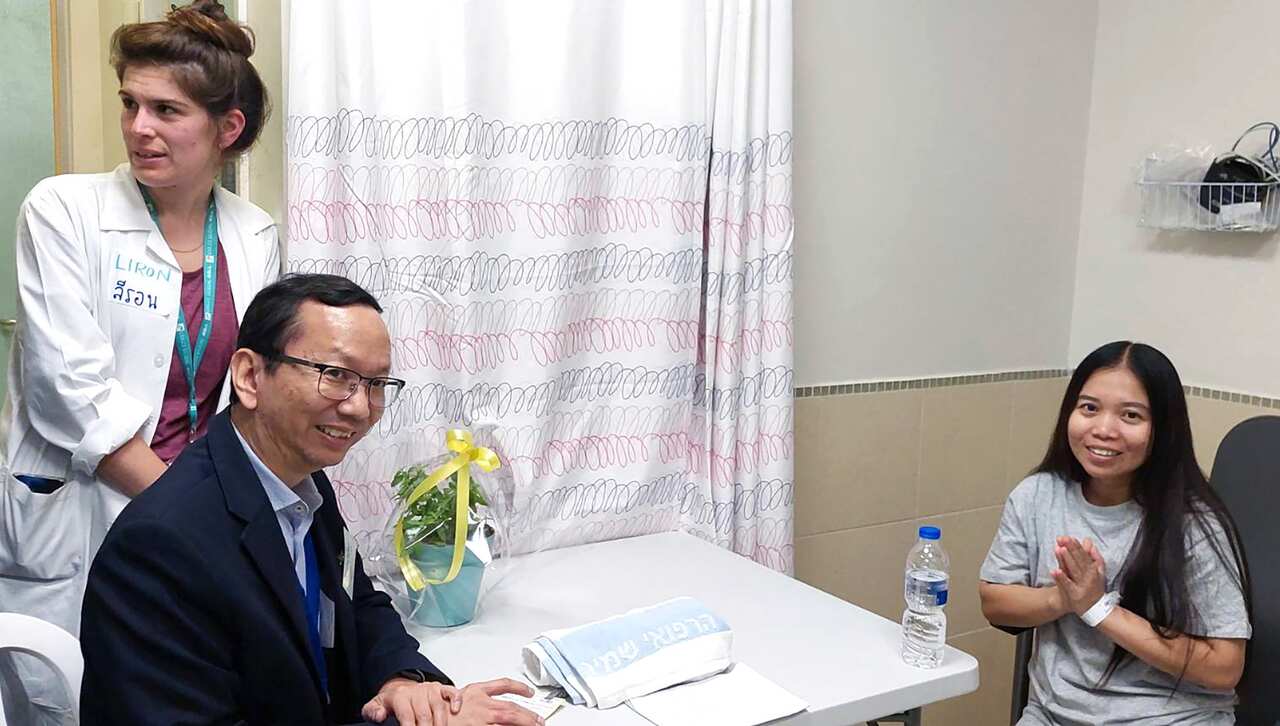 A Thai female migrant worker places her hands together in a sign of gratitude next to a Thai ministry official and an Israeli health officer. 