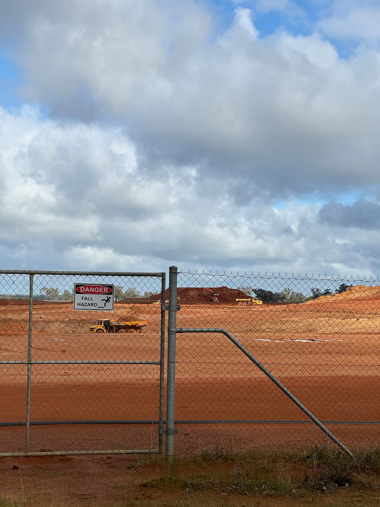 A fence with a sign that says Danger Fall Hazard in front of a pit of red dirt.