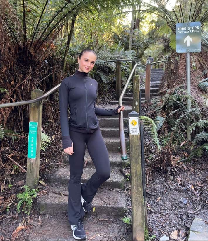 A woman in black active wear stands at the foot of a bush track.