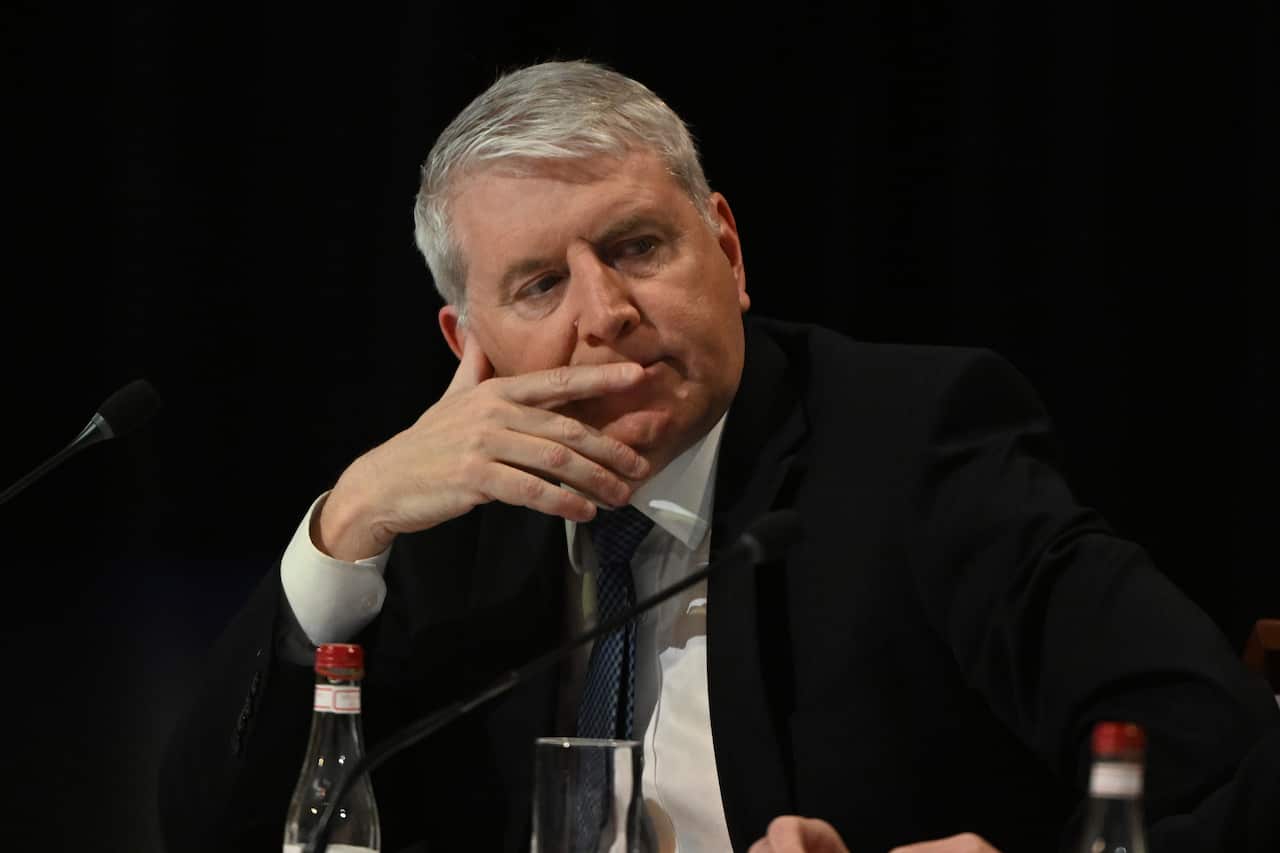 A man sits at a table with his hand partly covering his mouth