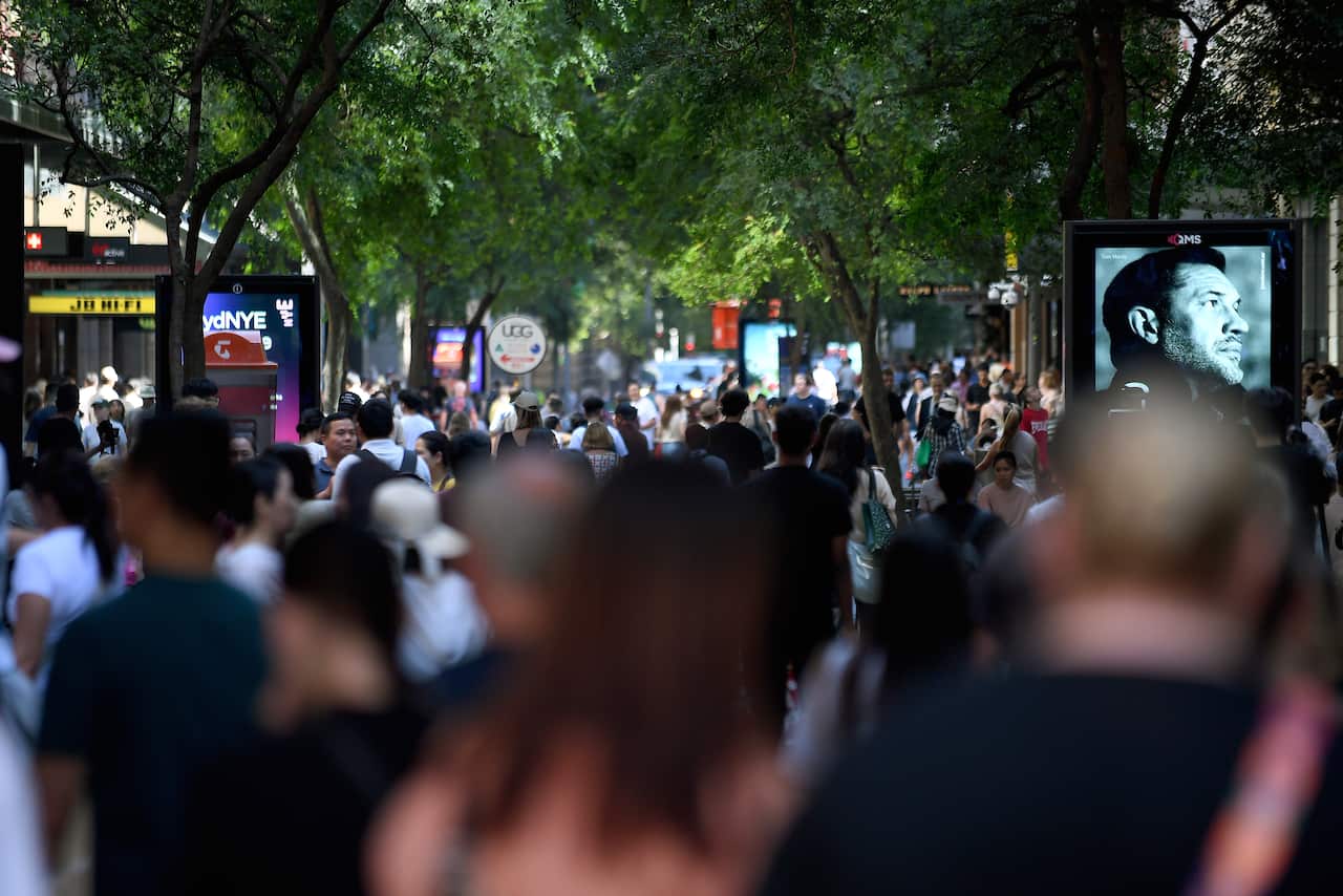 A large crowd of people moving through an outdoor shopping centre.