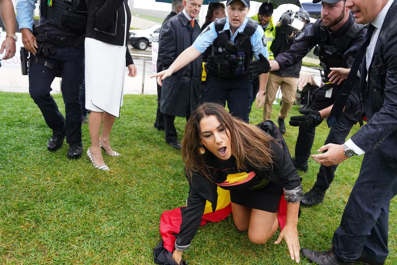 Woman in an Indigenous flag yells on the ground with security and police around her.