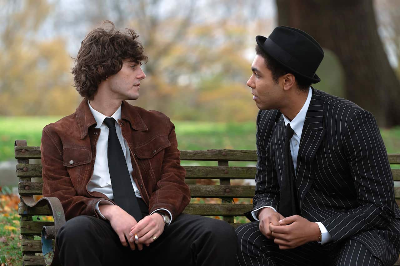 Two young men sit on a park bench, talking. 