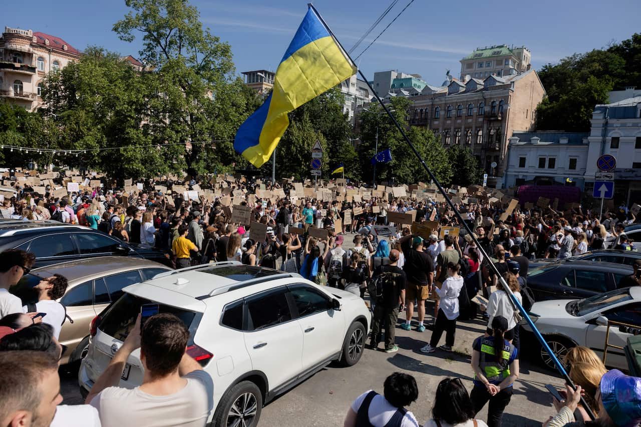 Protesters wave signs and Ukrainian flags in a town square.