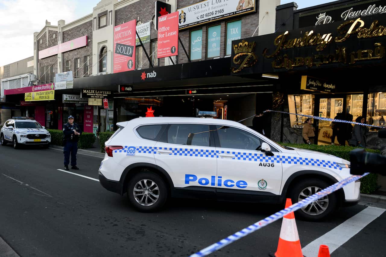 A police officer standing behind a police car in a taped off street 