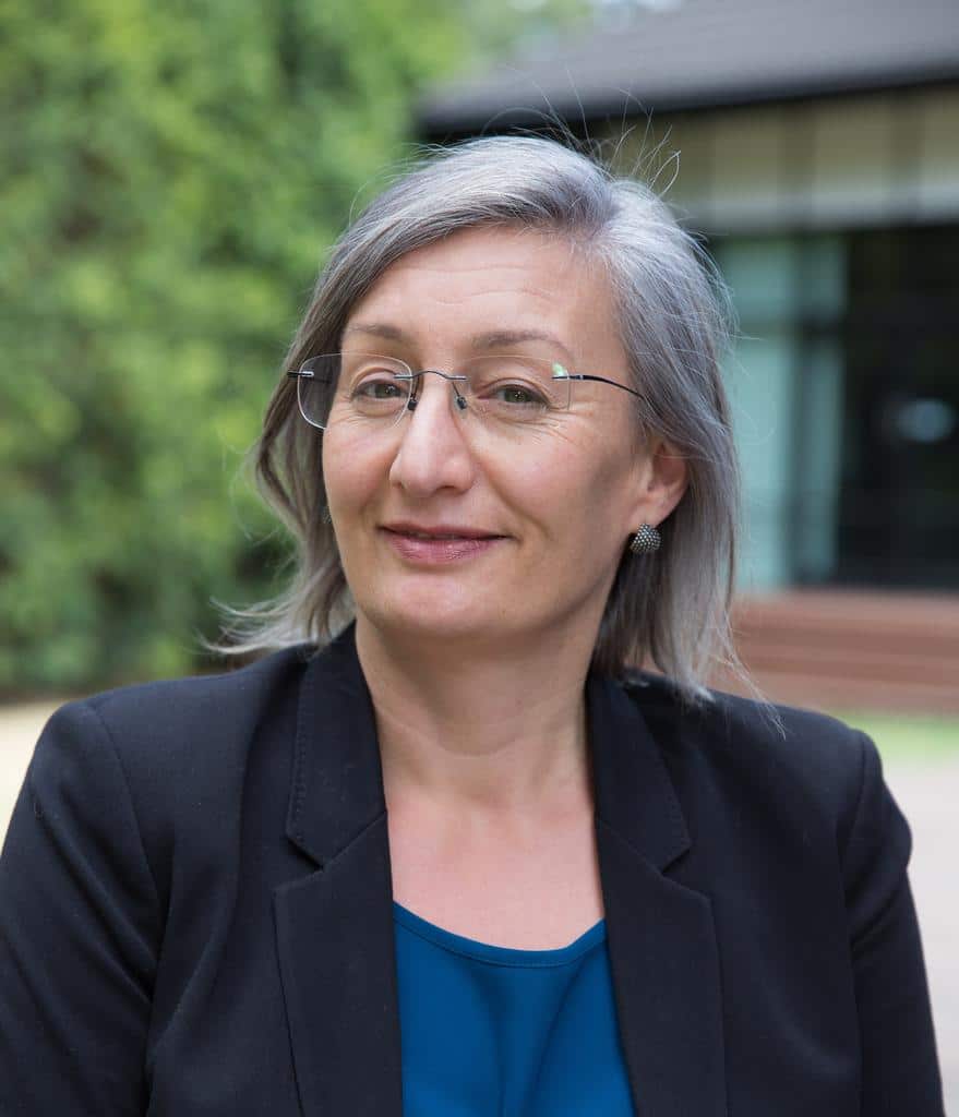 A woman with grey hair wearing a dark jacket and glasses