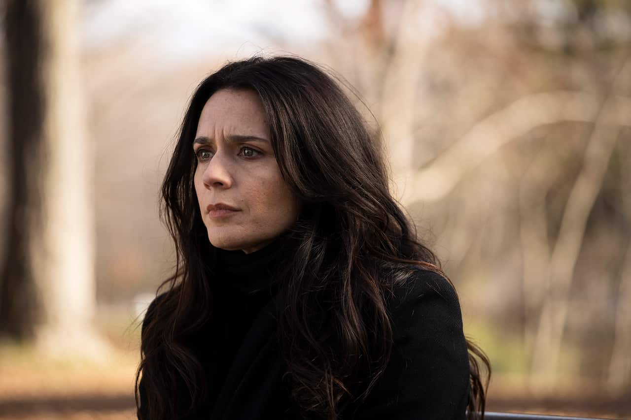 A woman in a dark jacket with long dark hair looks intently off to one side.