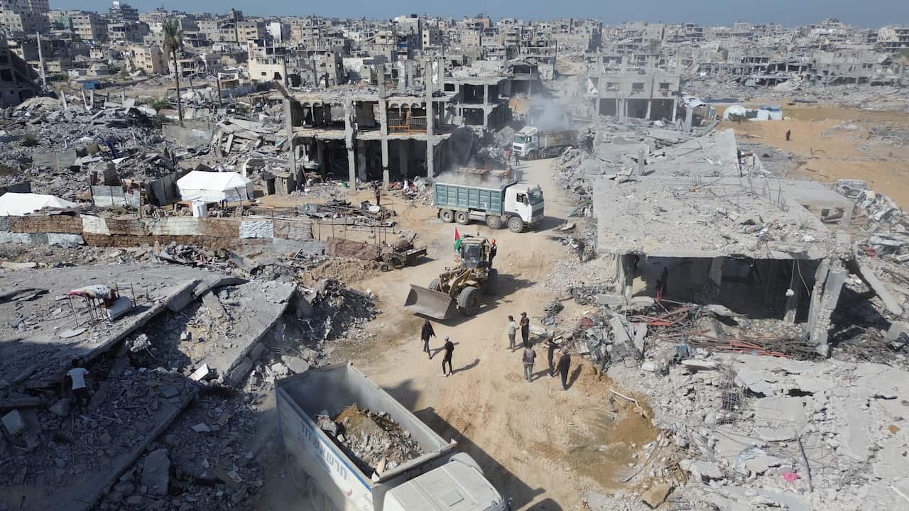People and vehicles clearing debris amid the rubble of heavily damaged buildings.