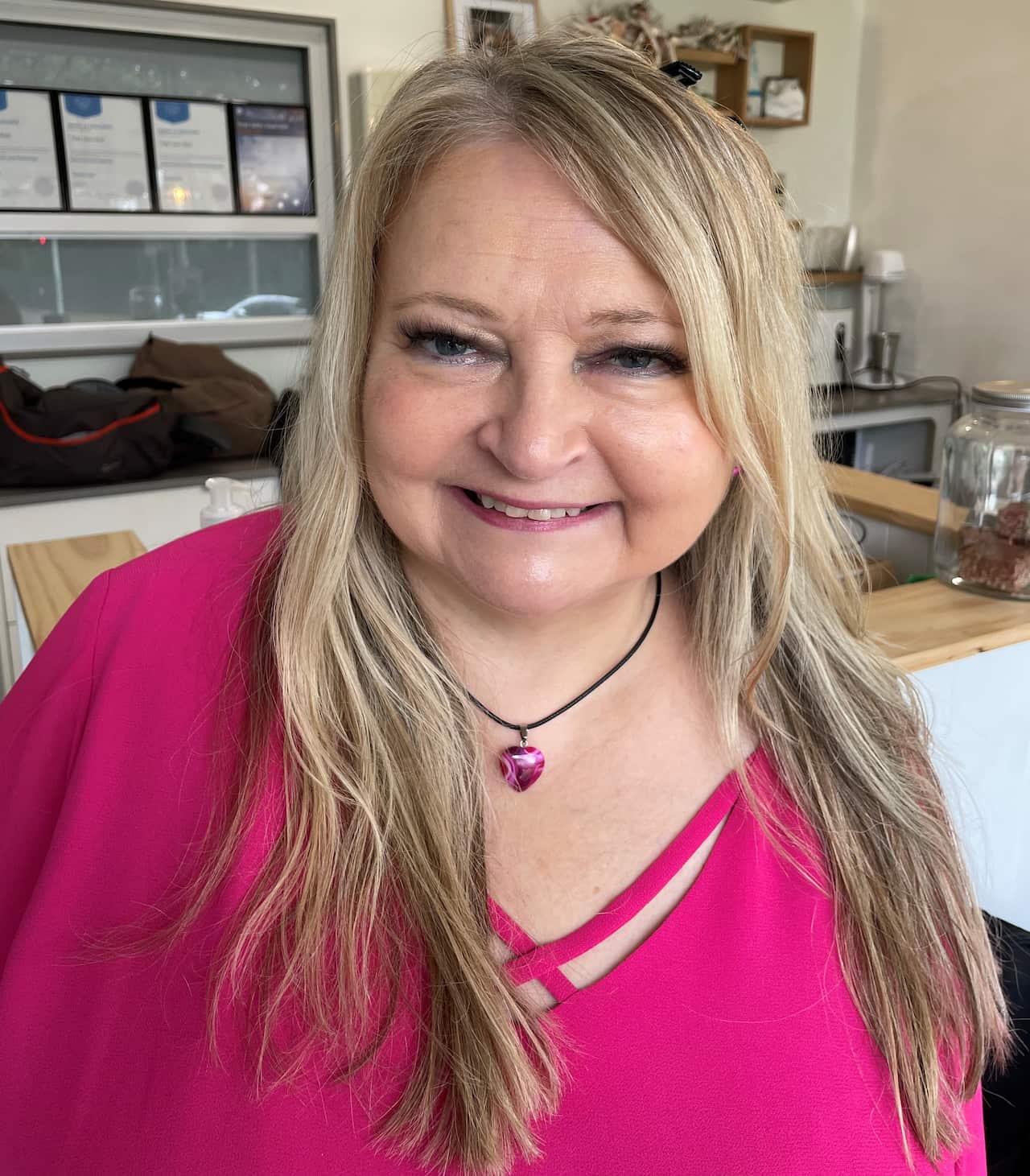 A woman with blonde hair wearing a pink top and smiling.