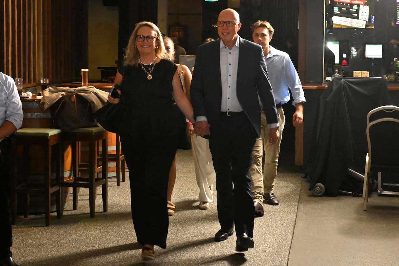 A man in a suit walks through a pub holding a woman's hand.