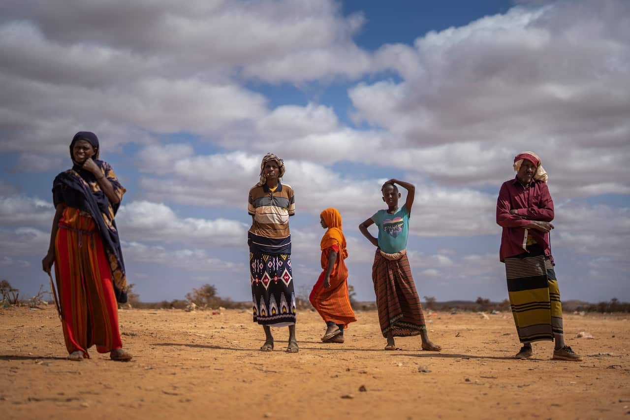 Men and women stand near a camp for displaced people in Somalia.