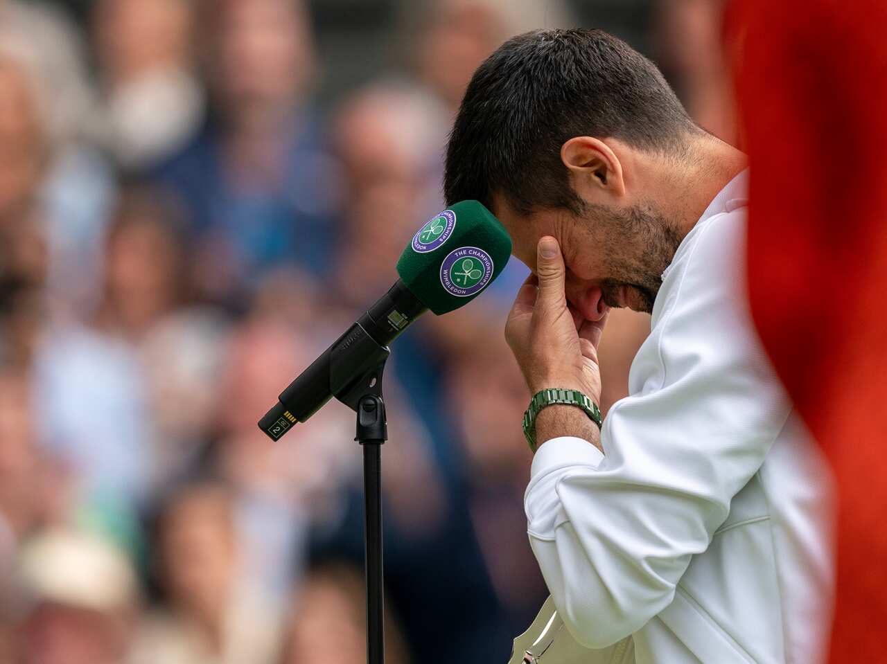 A man cries at a trophy presentation ceremony in front of a microphone.