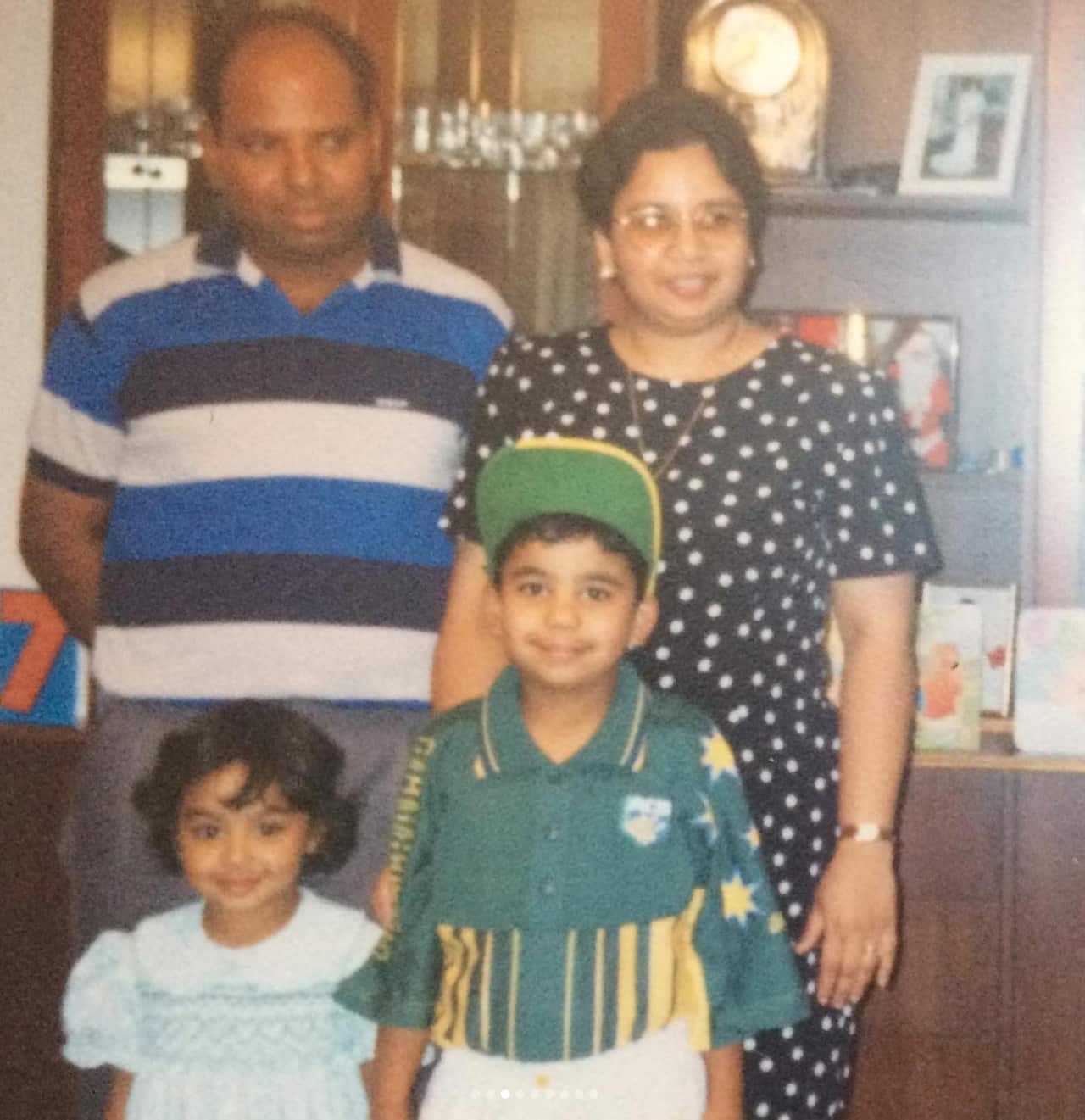 Family picture of mother and father with young son and daughter, standing inside 
