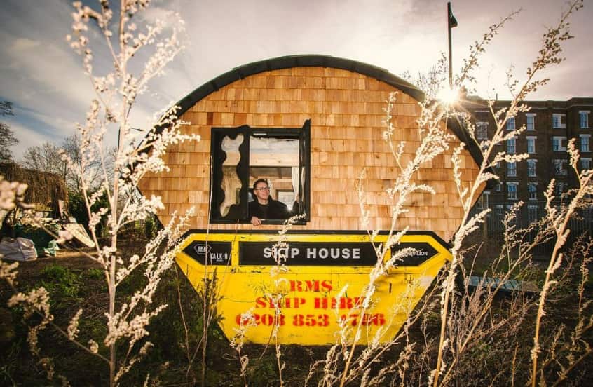 A man stands from the window of a skip. 