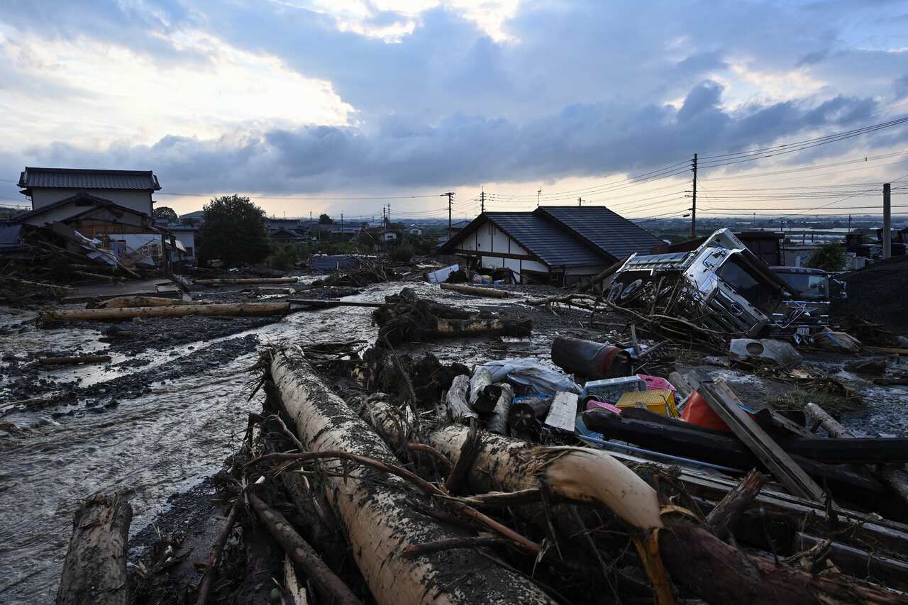 Fallen trees, debris, a vehicle on its side and inundated houses amid a flooded scene.