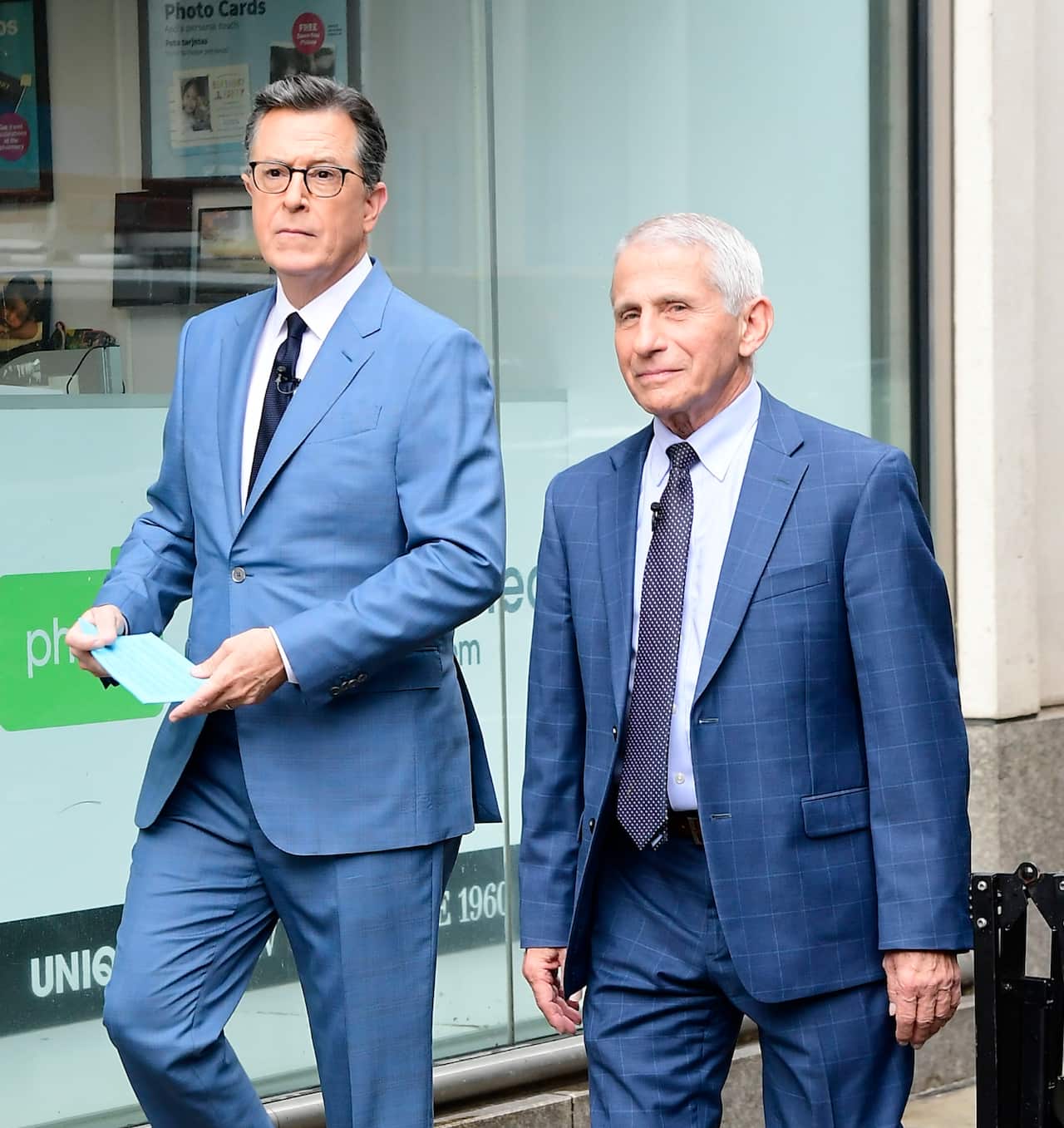 Two men in blue suits walk along a city street