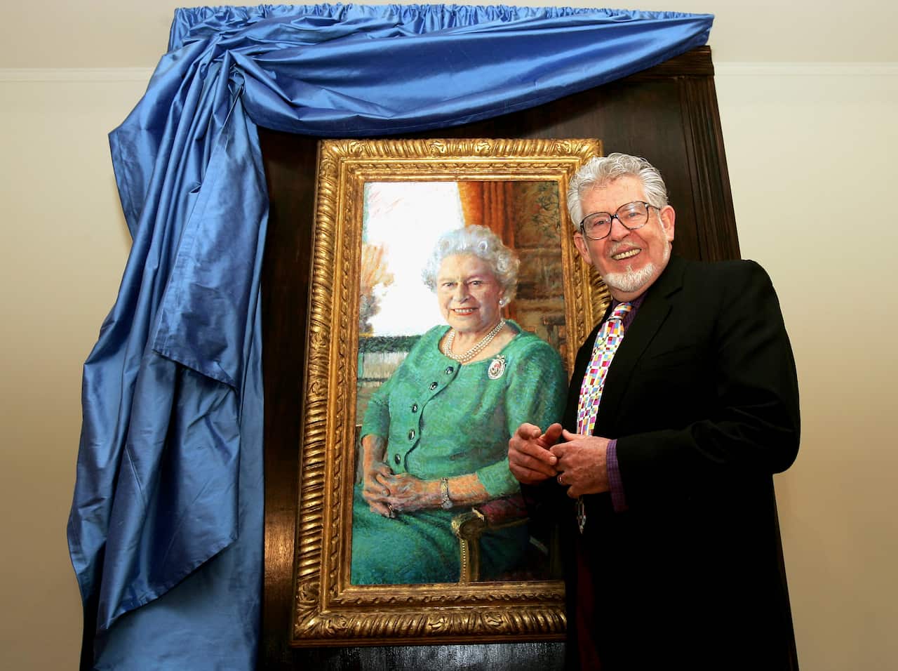 A man wearing a suit and tie standing next to a painting.