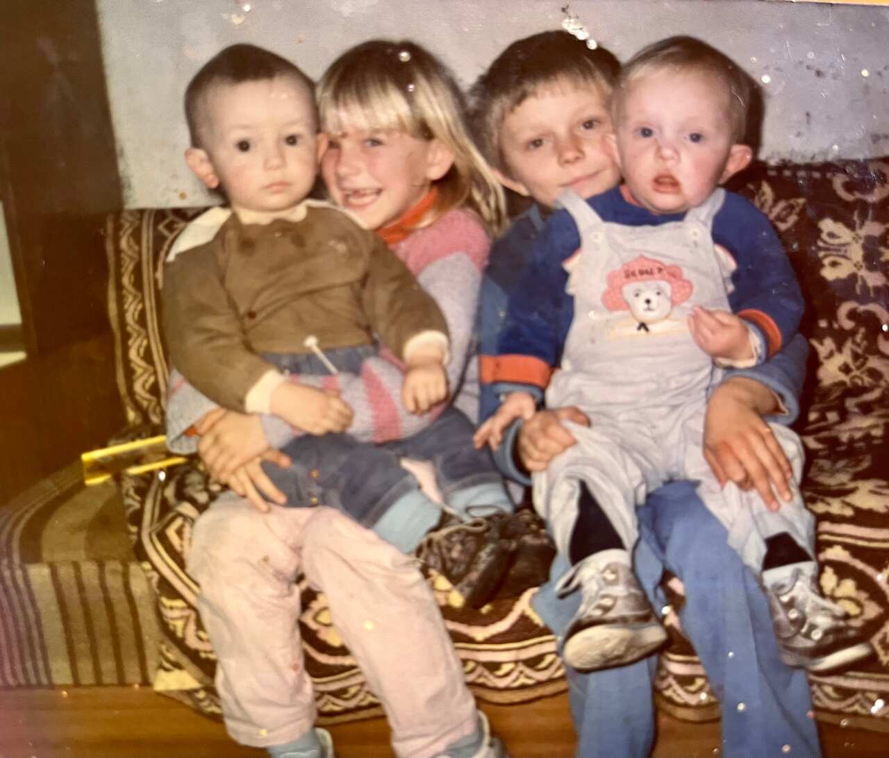Four children are seated on a printed couch  