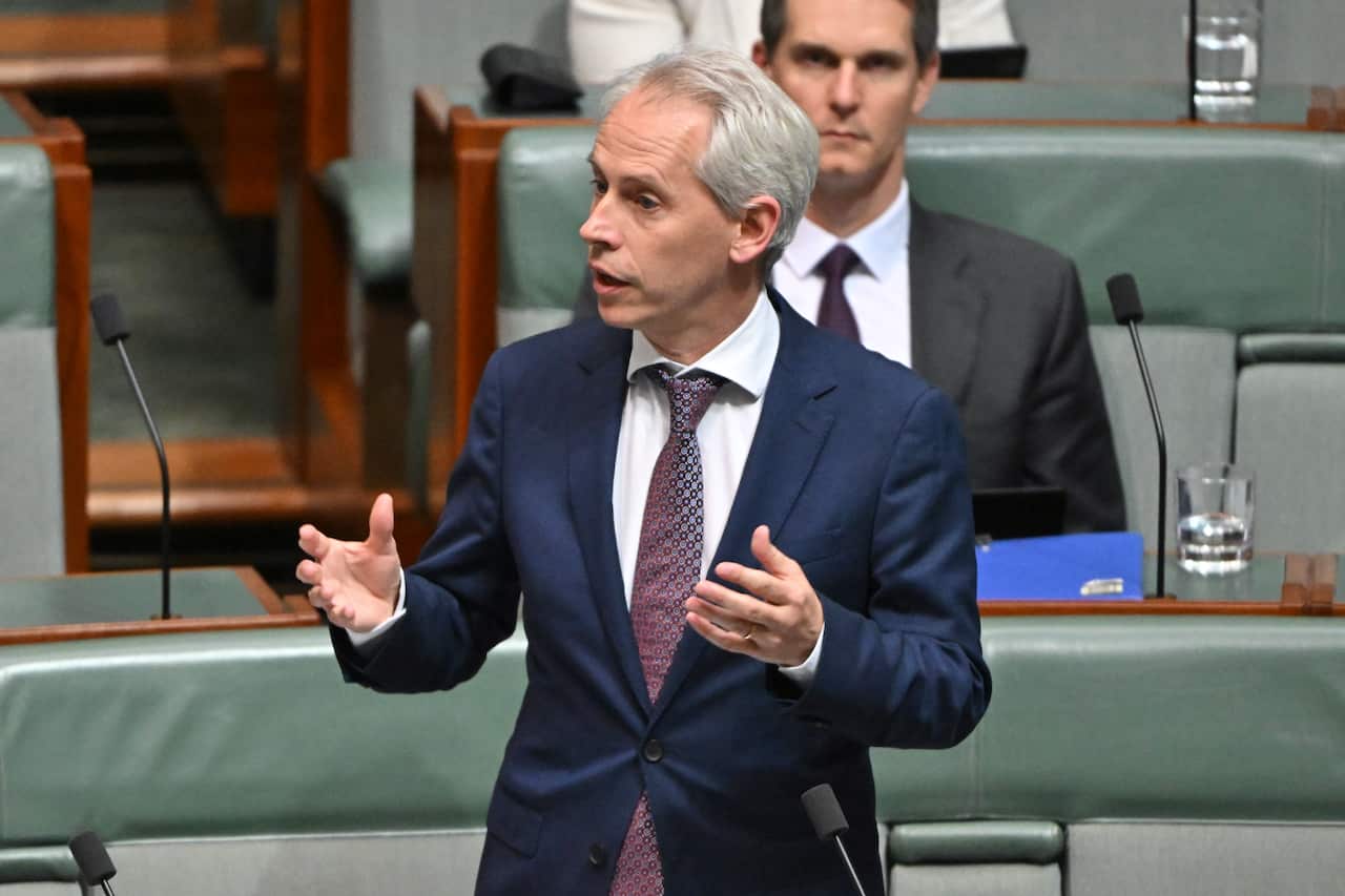 Man in a tie and suit gestures as he speaks in parliament.