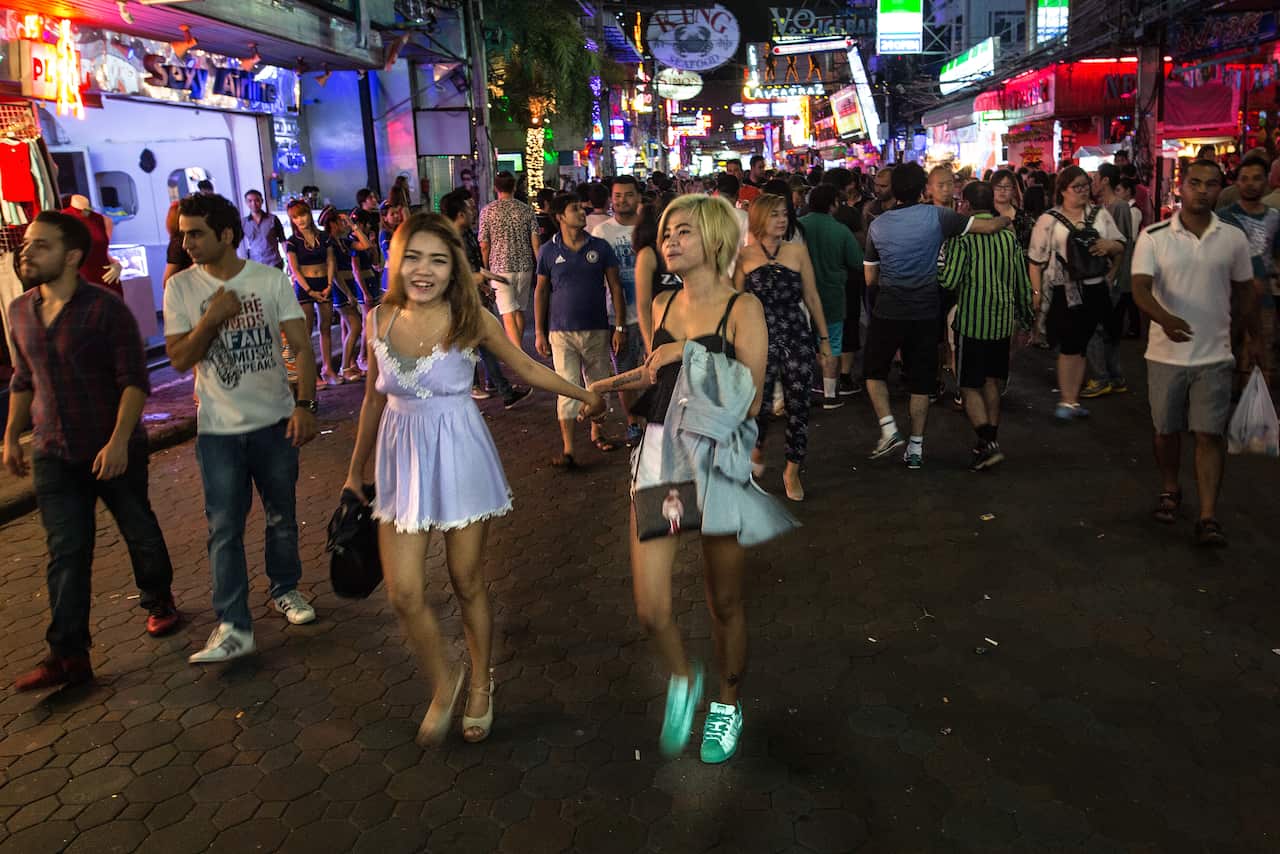 Two women holding hands walk down a crowded street
