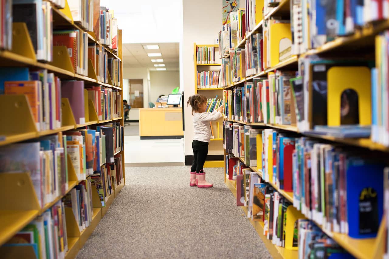 A small child looking at books in a library.