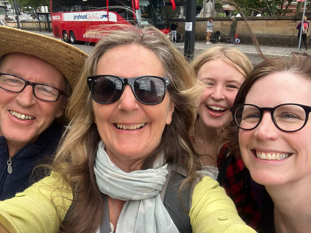 The Carols in Sydney, smiling at the camera, with a Greyhound bus in the background.