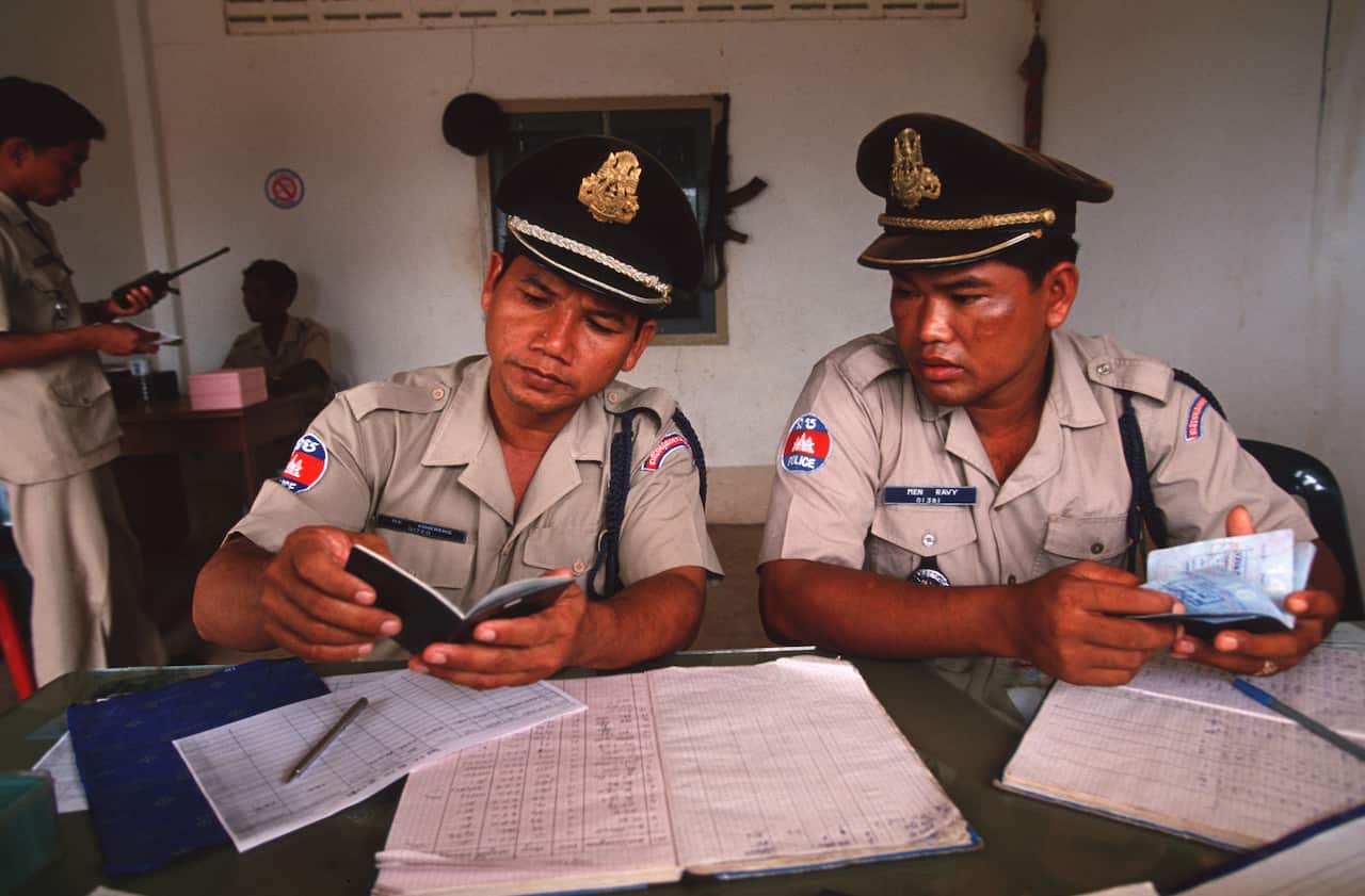 Two Cambodian border police officers  examine passports of people leaving.