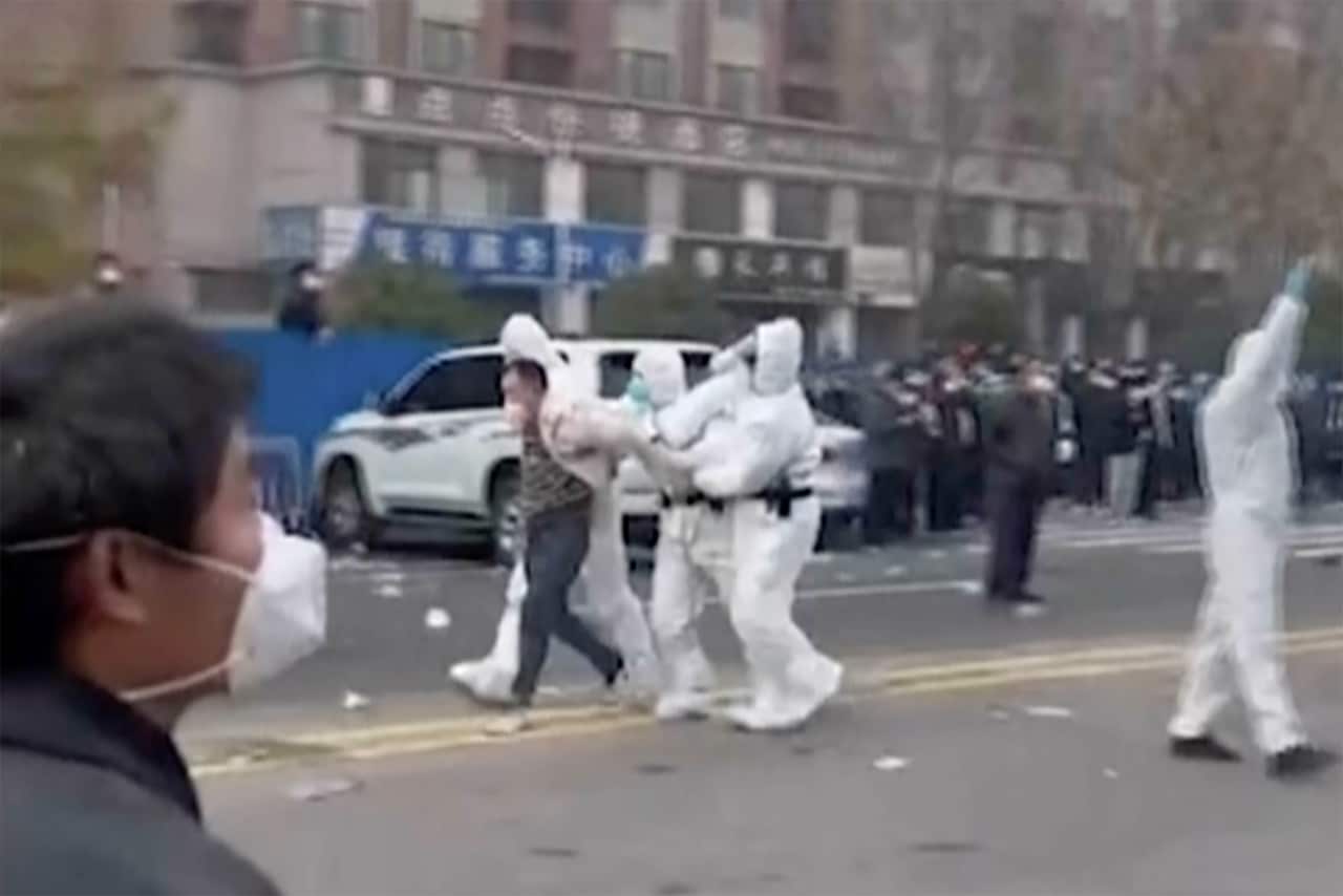 Man being arrested in the street by three people wearing white protective clothing.
