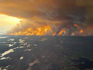 A massive fire on the horizon in a wild area, seen from a helicopter.