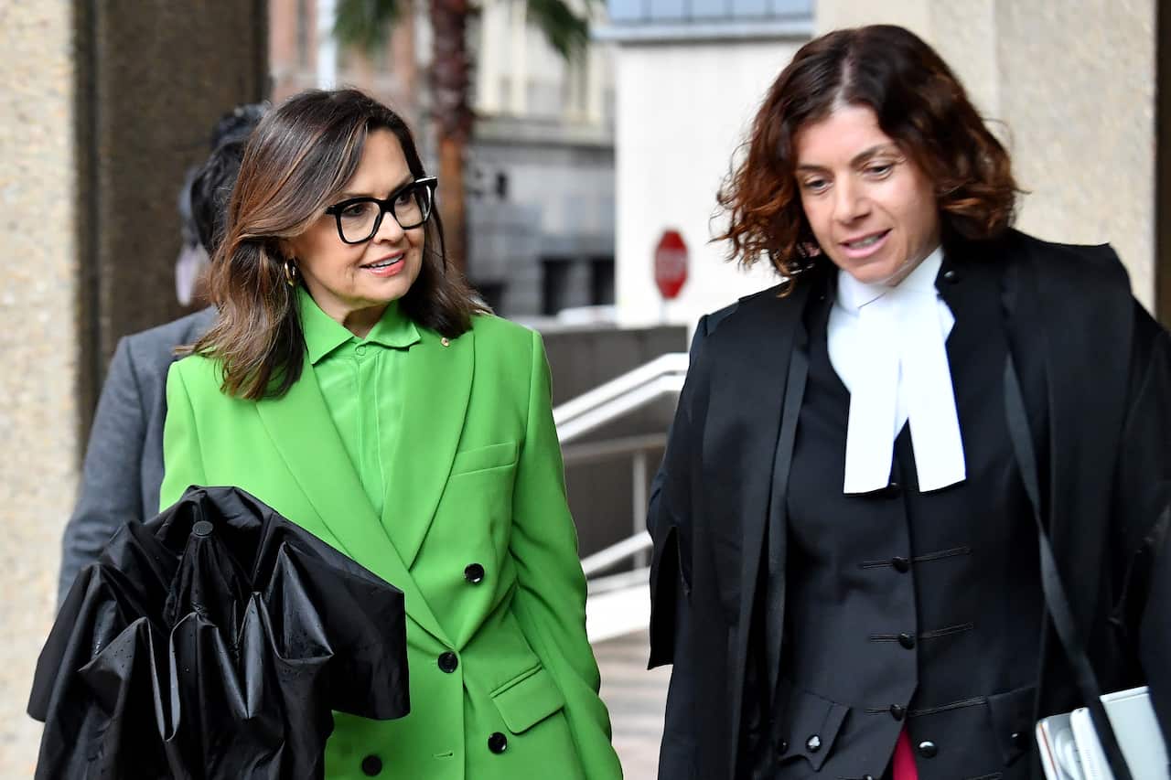 Two women walking outside. Lisa Wilkinson is wearing a green suit and another woman is in the attire of a barrister. 