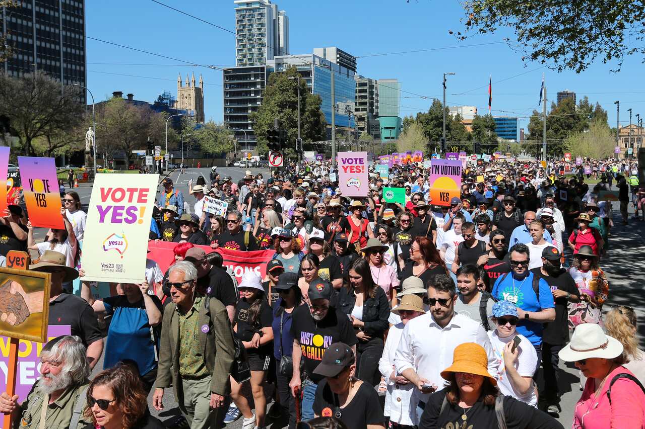 A crowd of people holding 'Vote Yes' placards walk through a street