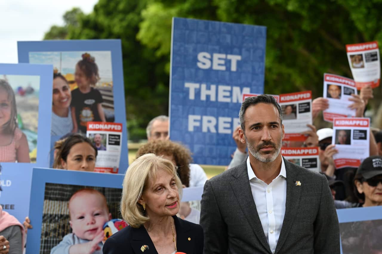 A man in a suit standing next to a woman. People are holding posters and placards behind them