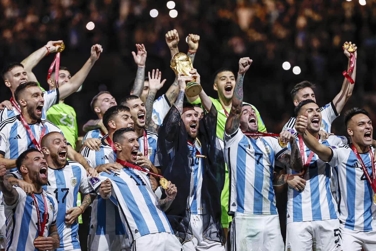 Football players dressed in blue and white striped jerseys celebrate as Lionel Messi holds up a golden trophy in celebration
