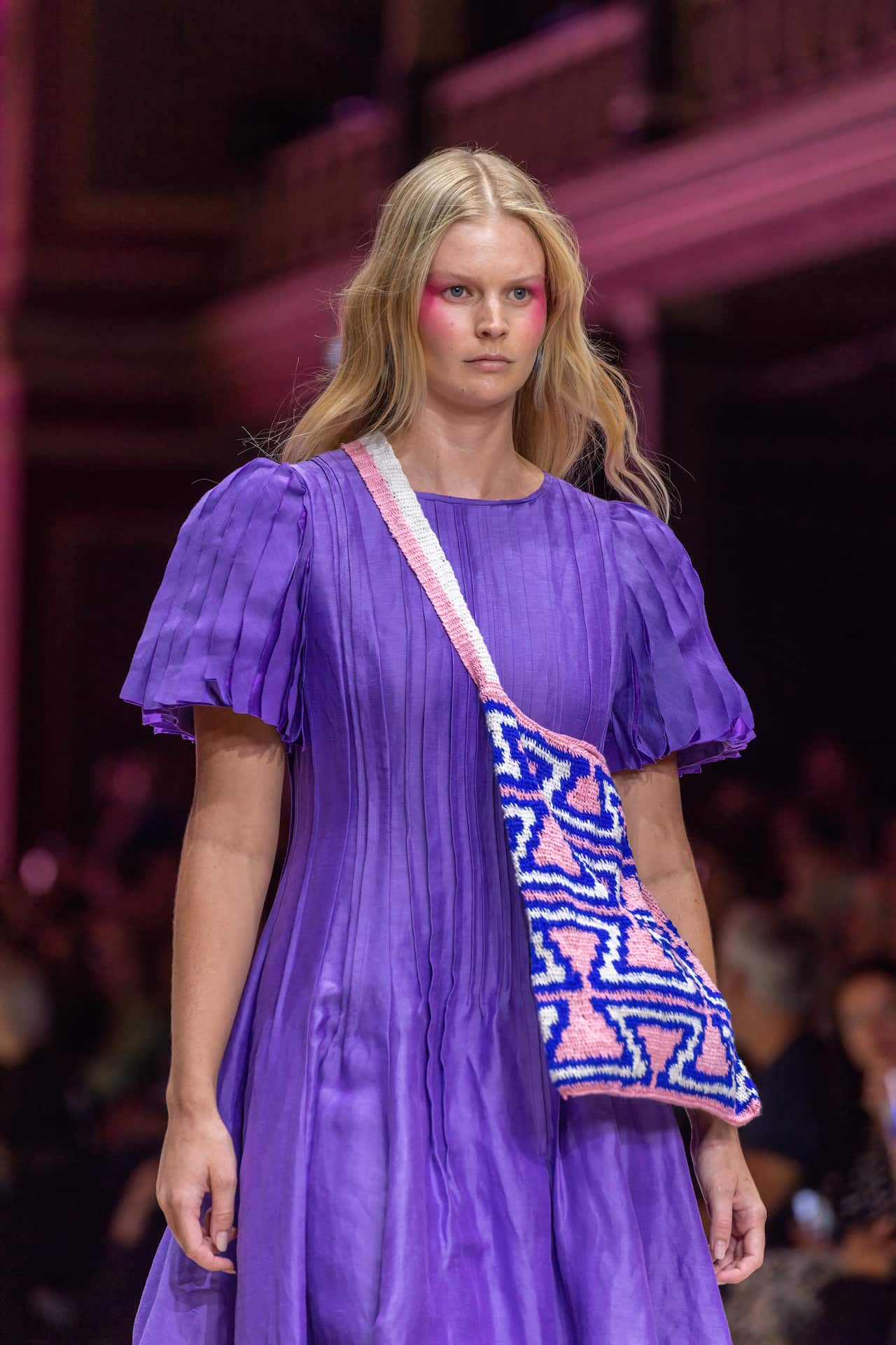 A blonde model in a purple dress walks the runway