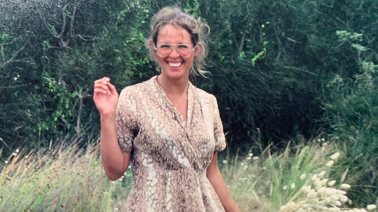 a young woman in glasses and a brown sun dress smiling in a field