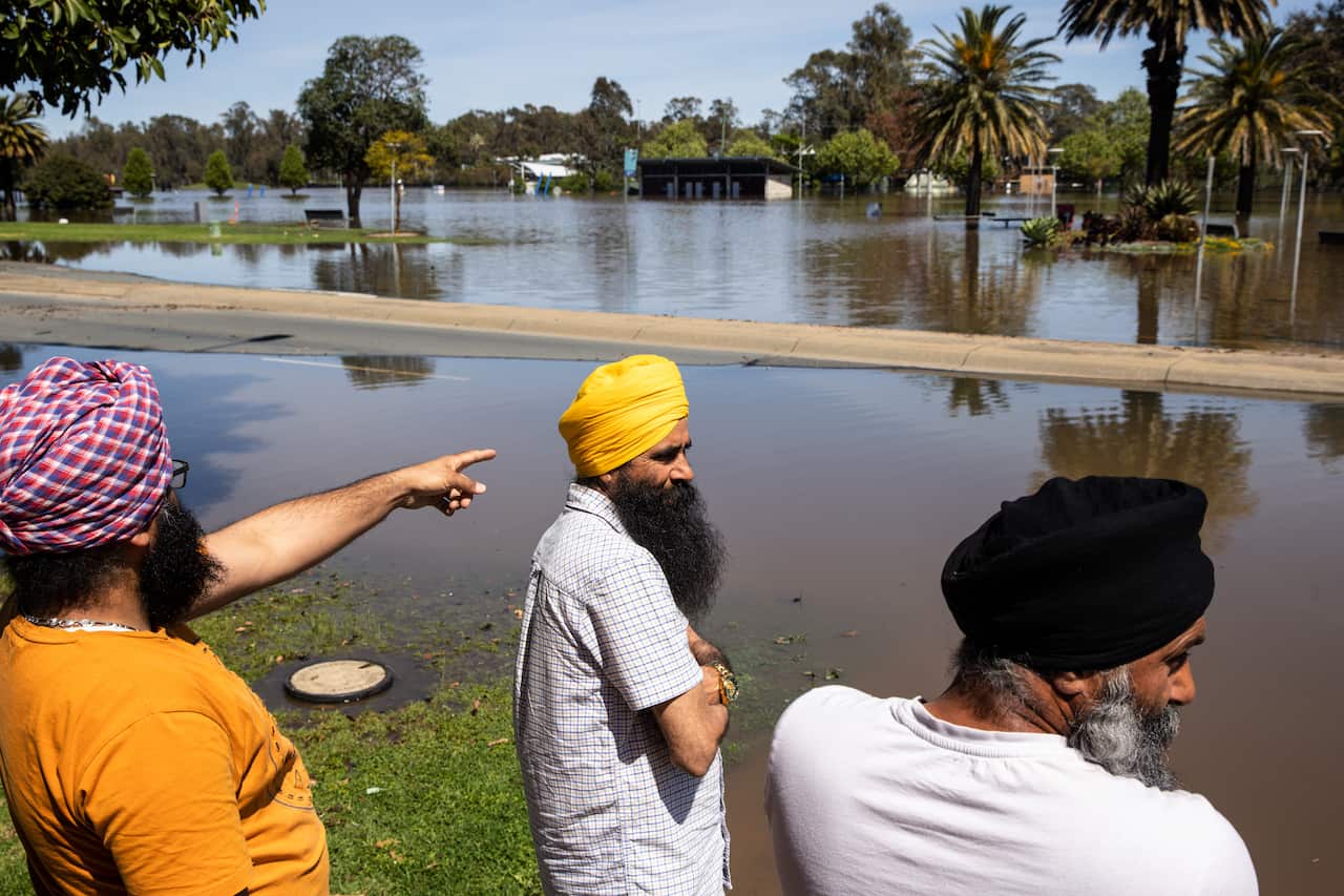 People look at floodwaters along a road