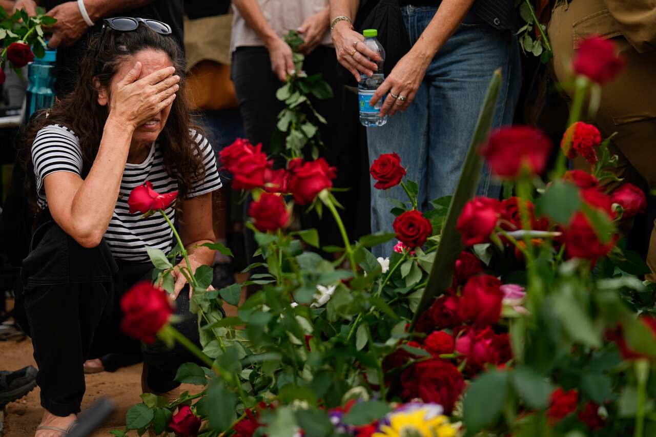A woman in a striped shirt squatting down and crying next to a rose bush.