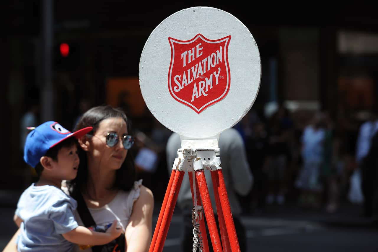 A woman carrying a child past a salvation Army wishing well.