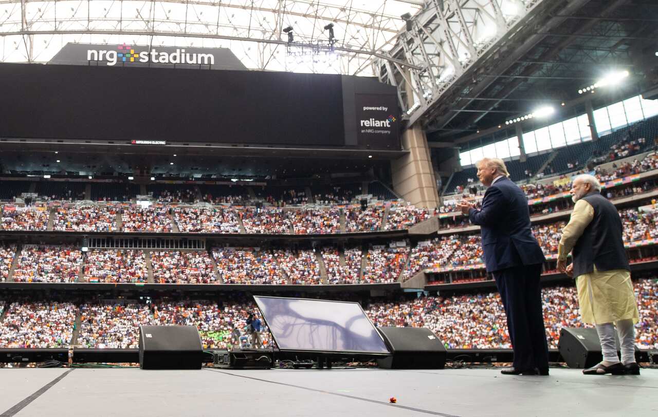 Two men on a stage address a packed stadium