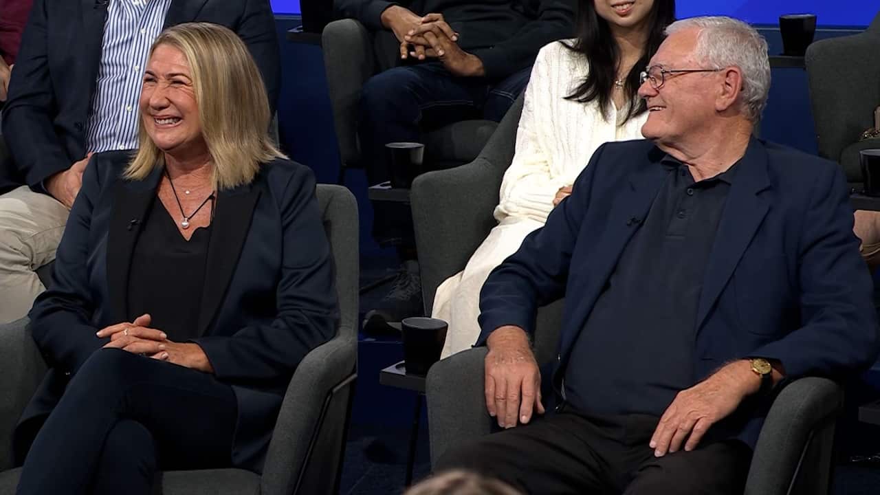 a midshot of a middle aged blonde woman and an older man with grey hair smiling sitting in a studio audience