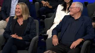 a midshot of a middle aged blonde woman and an older man with grey hair smiling sitting in a studio audience