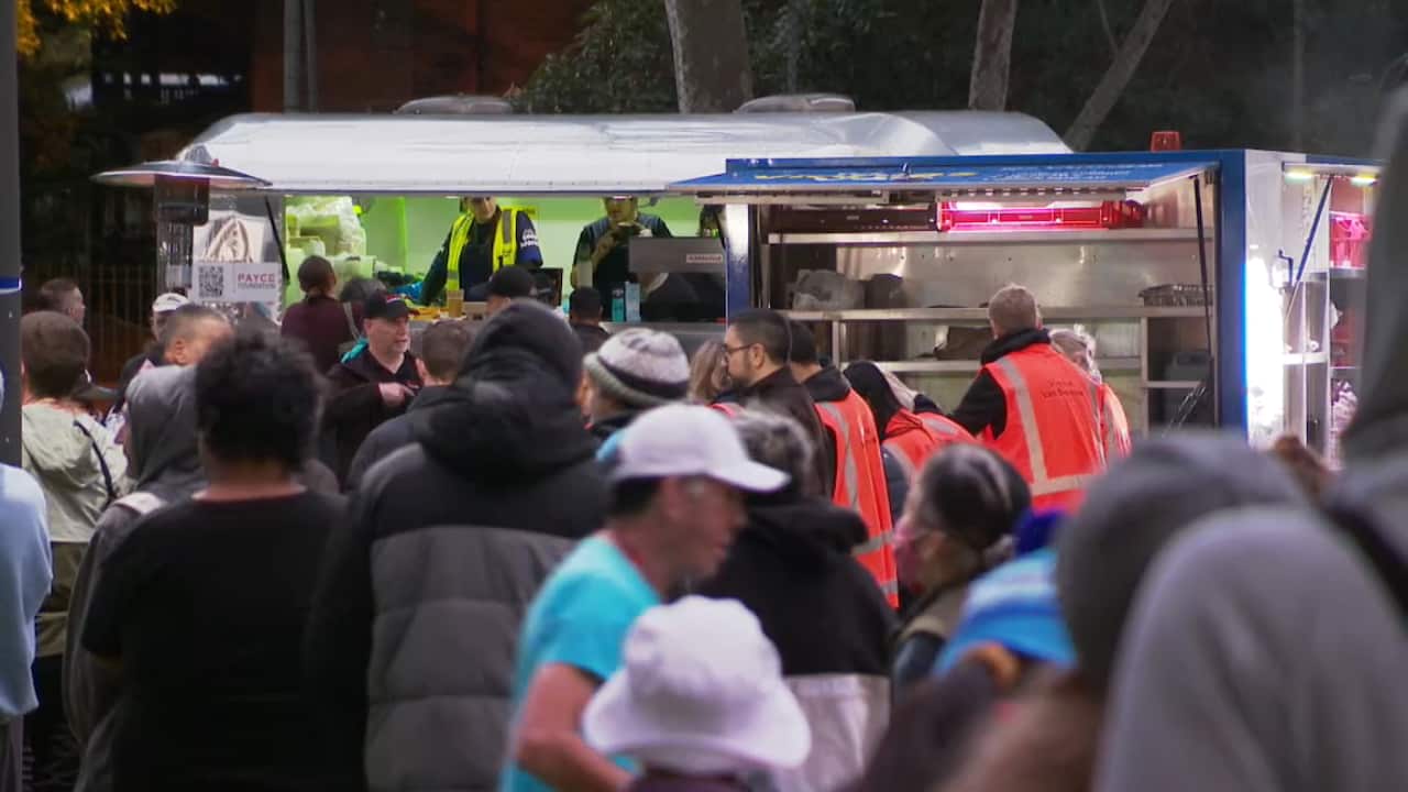 A crowd of people queue to collect food from vans at a Homelessness Week event in Sydney.