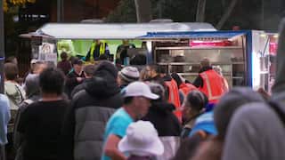 A crowd of people queue to collect food from vans at a Homelessness Week event in Sydney.
